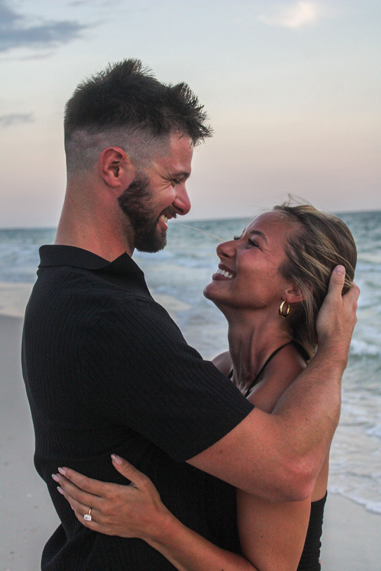 Couple laughing together with a man holding a woman’s head beside the ocean by Miranda Rae Photography