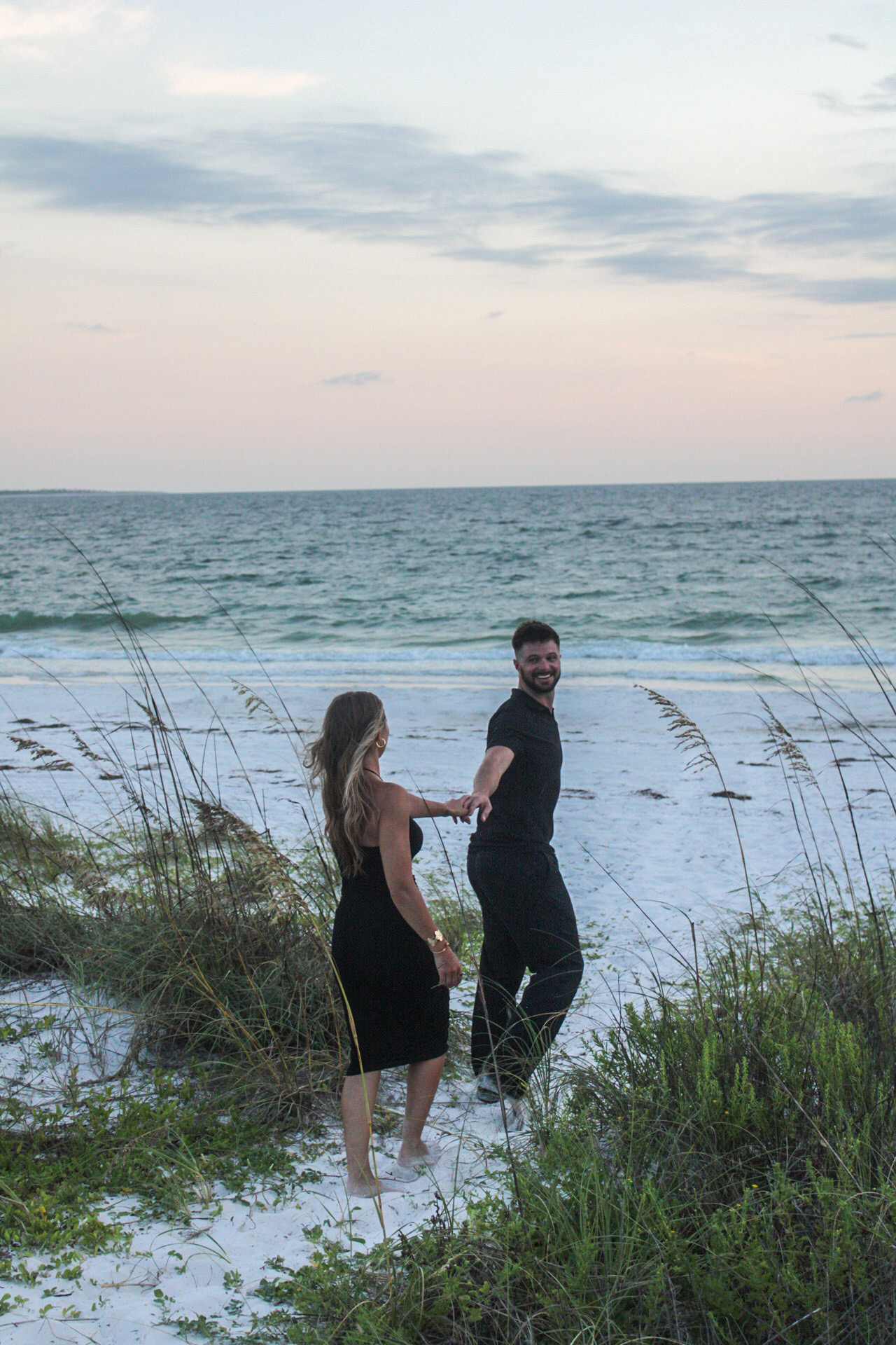 Couple holding hands on a sandy path through the dunes by Miranda Rae Photography