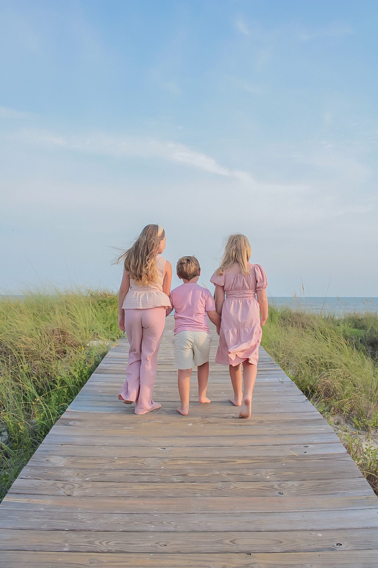 Three children in pink walking away along a boardwalk by Miranda Rae Photography