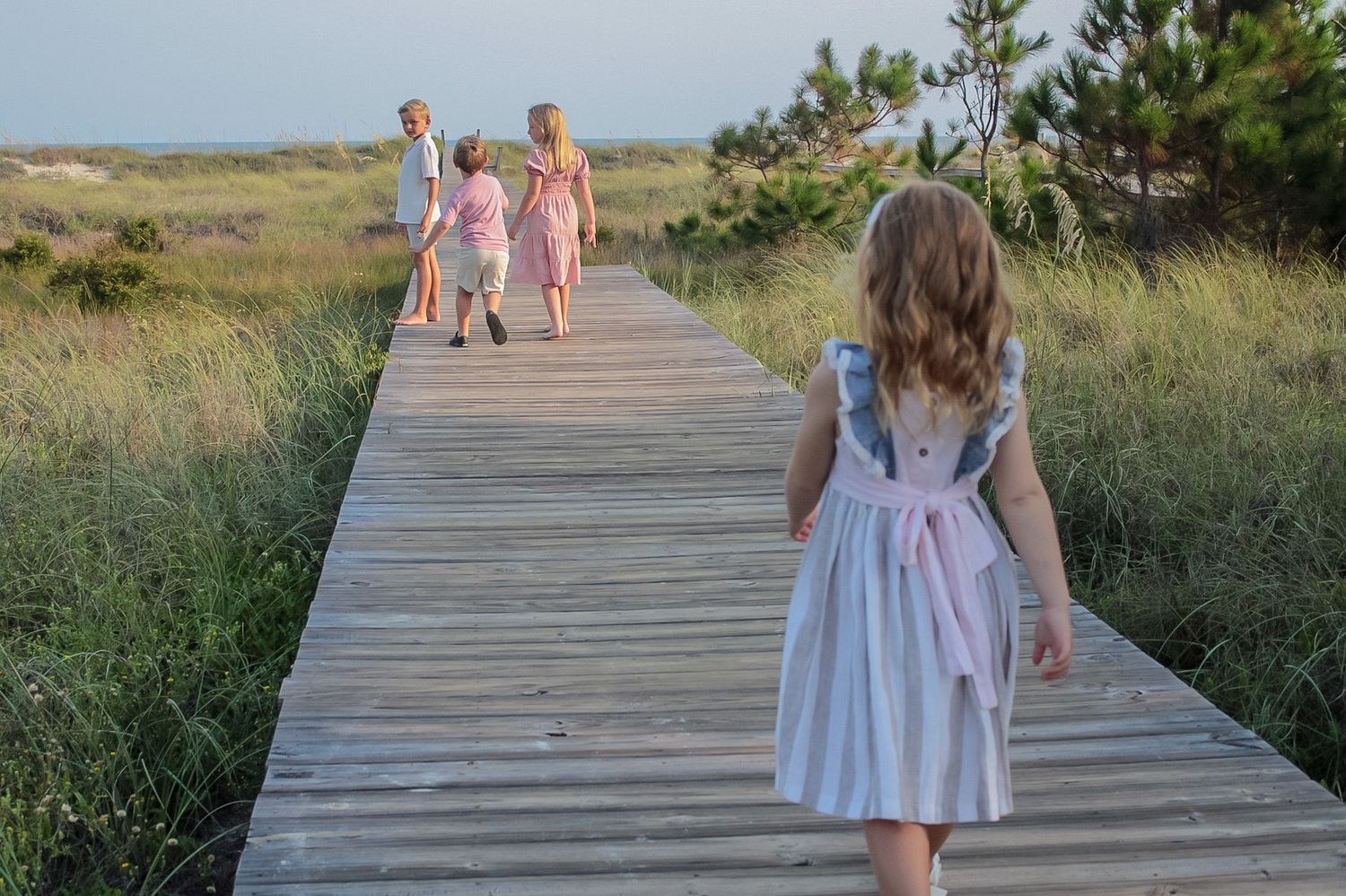 Little girl walking a beach boardwalk toward her siblings at Cape San Blas by Miranda Rae Photography