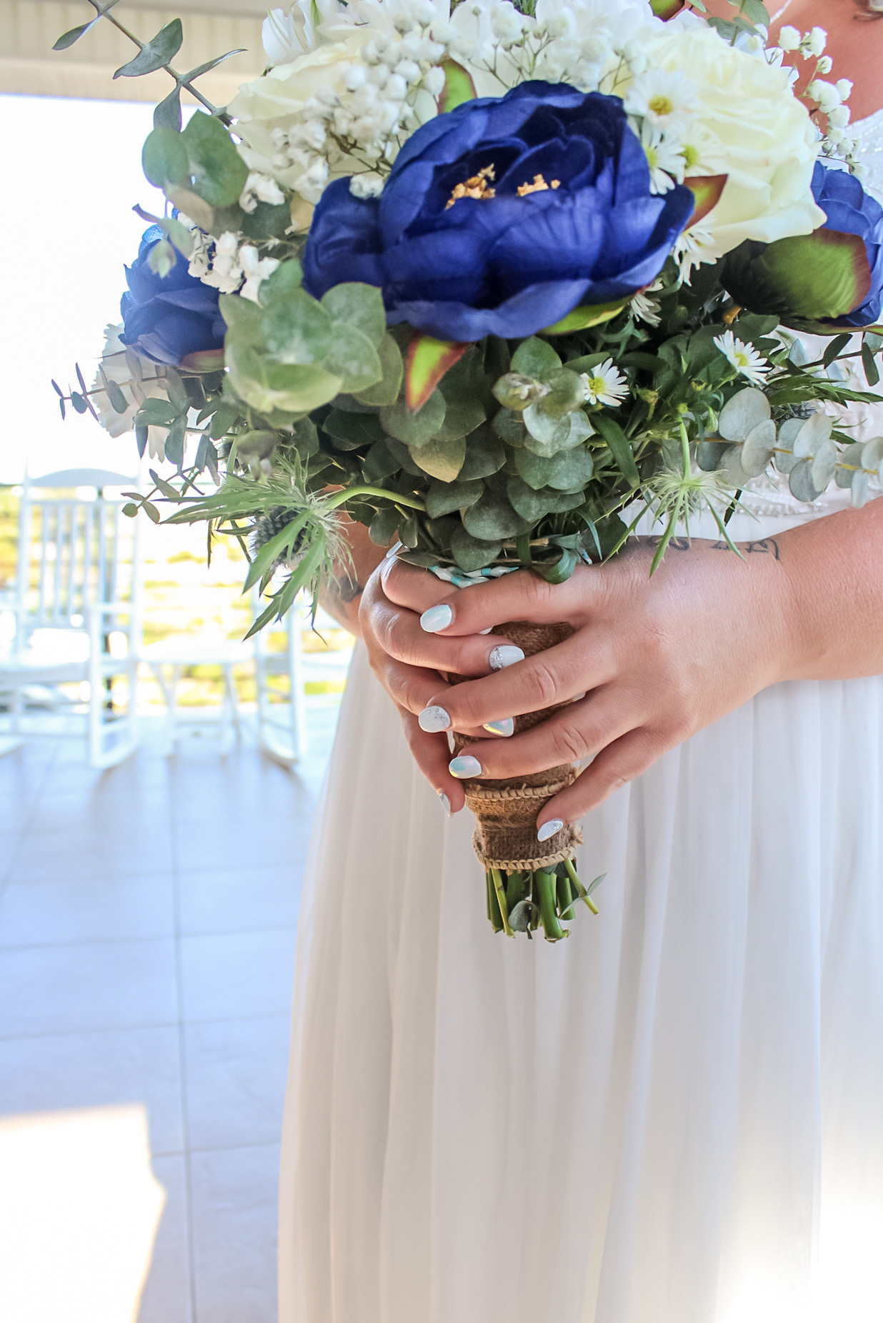 Blue and white bridal bouquet held against a white dress