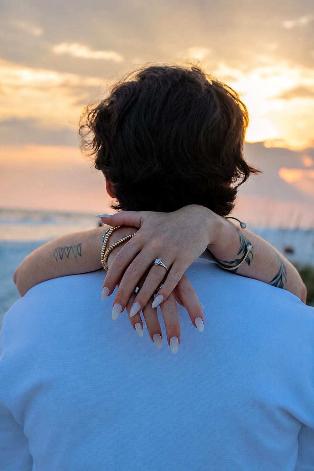 Engagement ring visible as a couple embraces at sunset