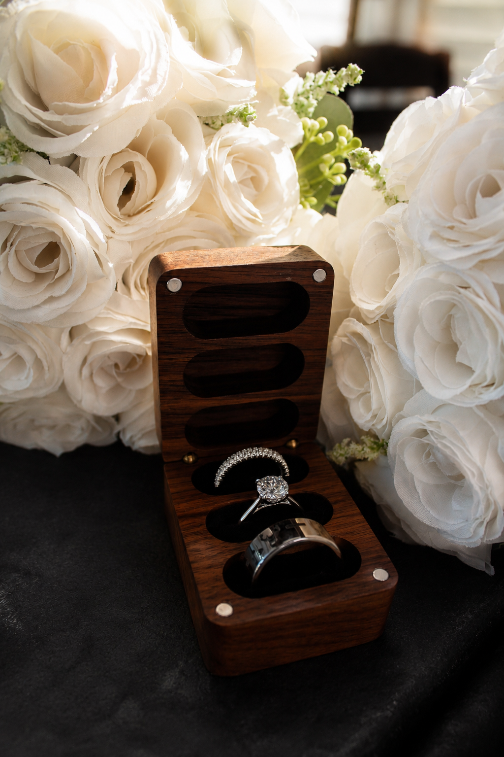 Wedding rings displayed in a wooden ring box among white flowers