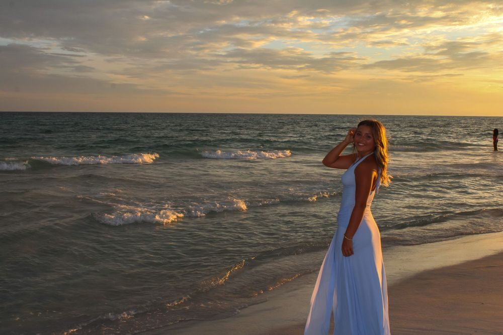 Woman in a long blue dress standing beside the surf at sunset by Miranda Rae Photography
